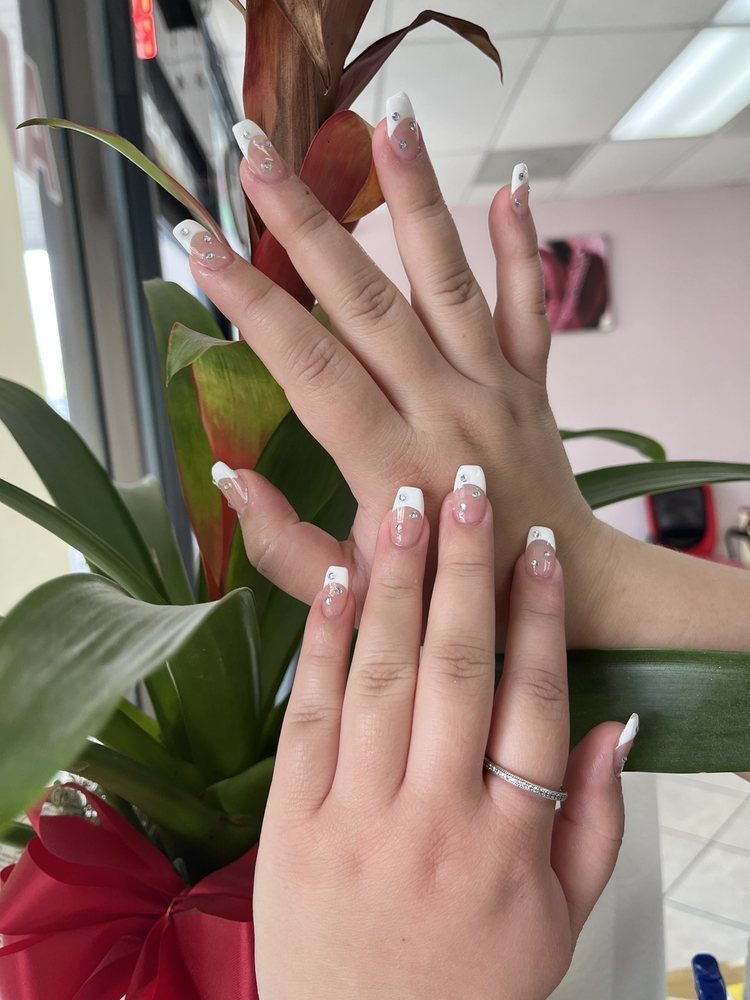 French tip manicure with crystal accents against a green plant at Aborn Nail.