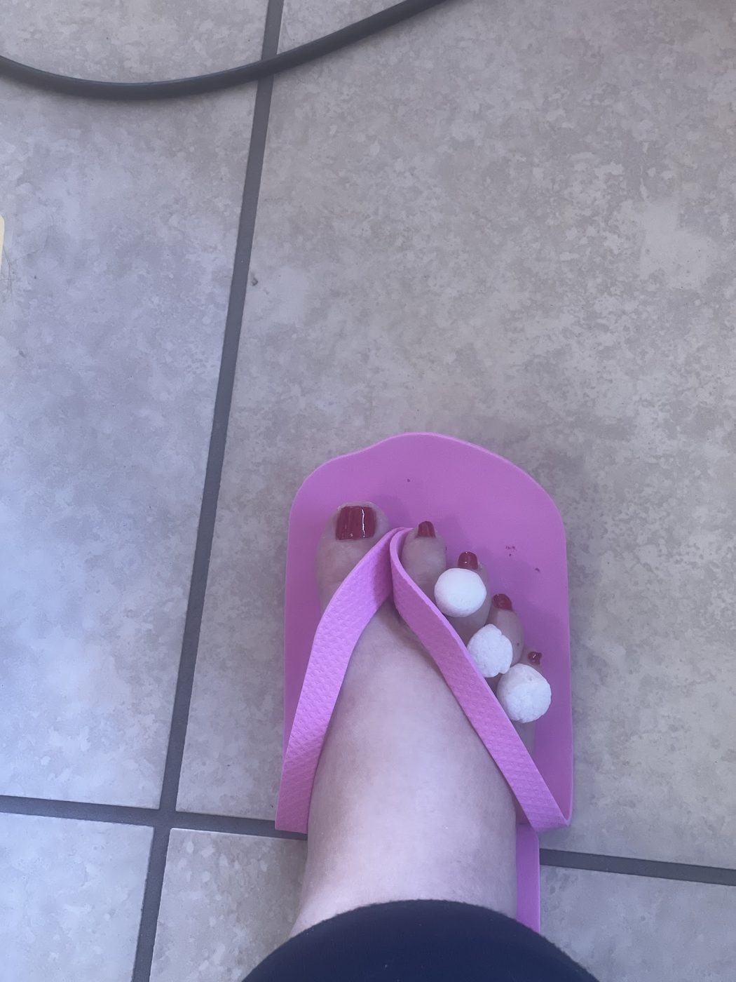 Burgundy pedicure in a pink salon foam slipper with toe separators.